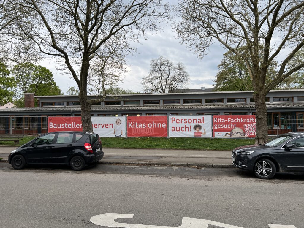 Bauzaunbanner am Kita-Neubau in Böblingen mit der Botschaft „Baustellen nerven – Kitas ohne Personal auch! Kita-Fachkräfte gesucht“ und QR-Code