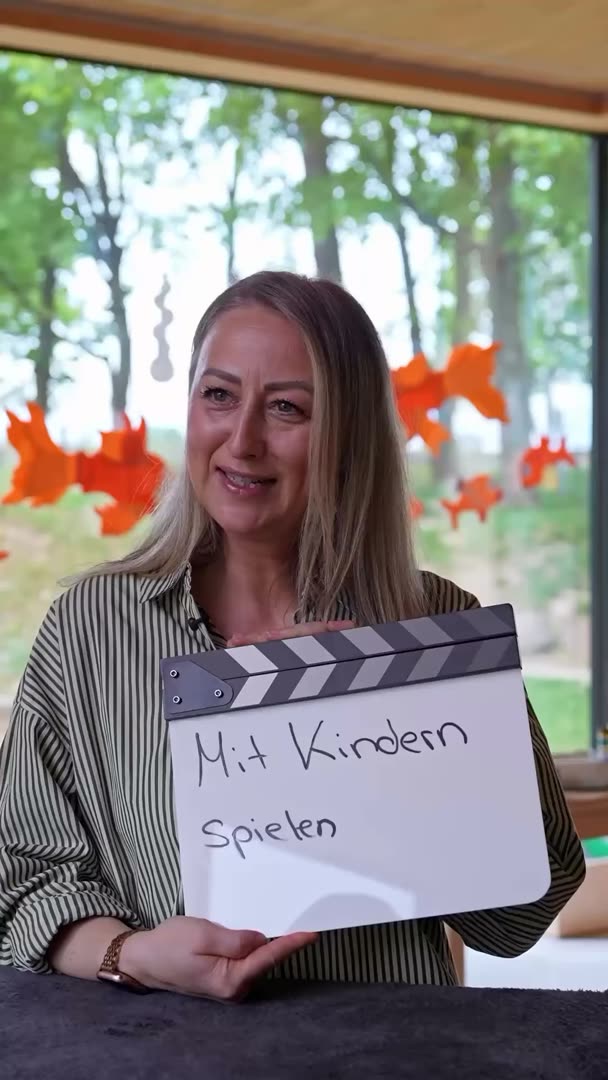 Erzieherin der Stadt Filderstadt hält eine Filmklappe mit der Aufschrift „Mit Kindern spielen“, Kurzvideo Soziales