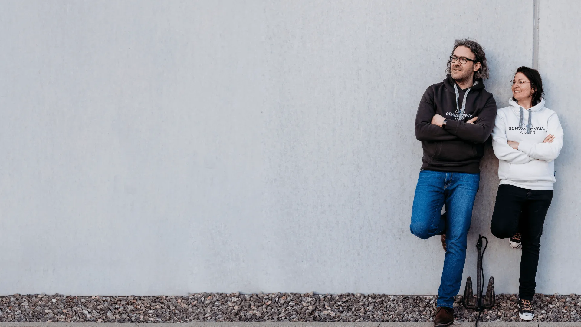 Adina und Arne Kocher von Schwarzwald Anker, Personalmarketing aus dem Schwarzwald, lehnen an einer Betonwand