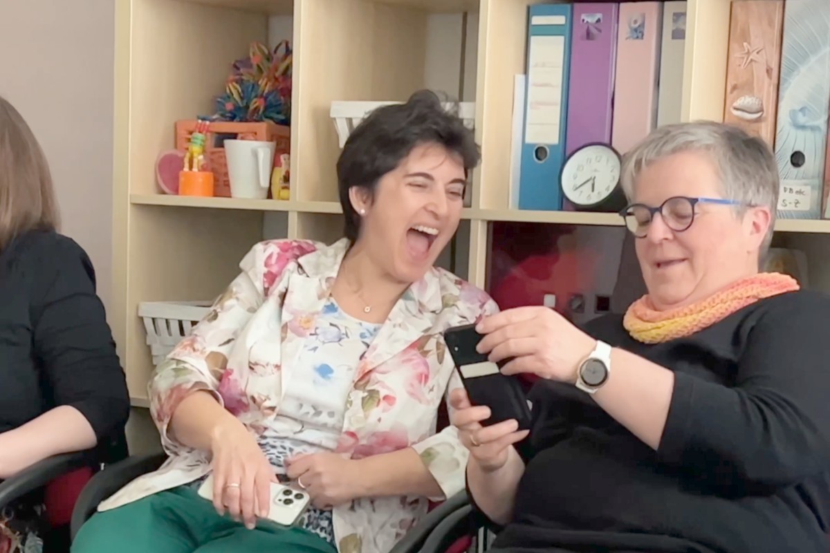 Zwei Teilnehmerinnen schauen sich lachend ihr eigenes Video auf dem Smartphone an