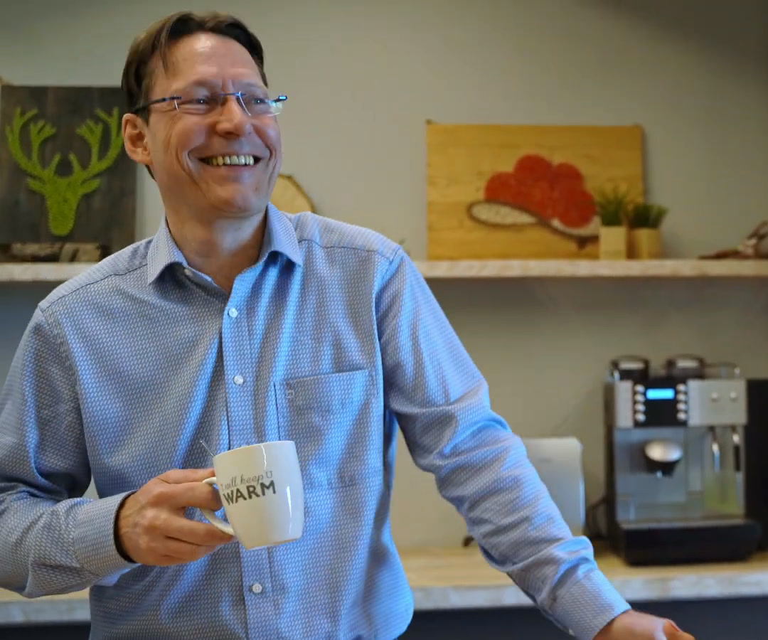 Mitarbeiter von hitcom lacht mit Kaffeetasse in der Teeküche, Szene aus seinem Mitarbeiter-Testimonial