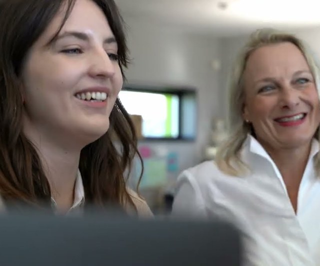Zwei Mitarbeiterinnen von hitcom lachen am Arbeitsplatz