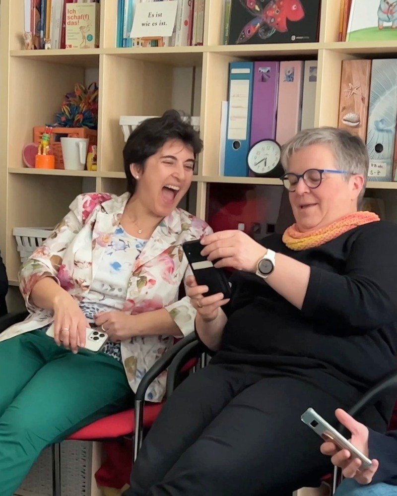 Zwei Teilnehmerinnen schauen im Videopraxis-Workshop lachend ihr eigenes Video auf dem Smartphone an